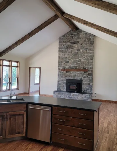 An empty kitchen with wood beams and a stone fireplace.