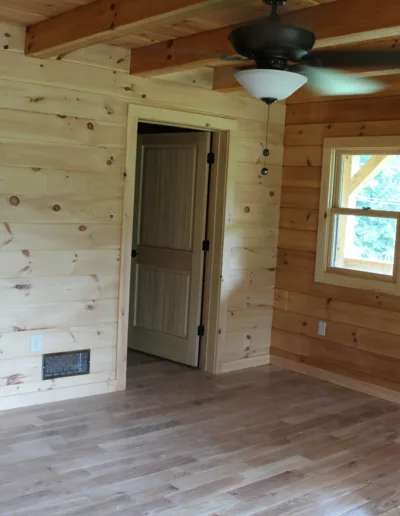A room in a cabin with wood floors and a ceiling fan.